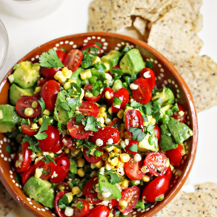 tomato avocado corn salad in a red bowl surrounded by tortilla chips