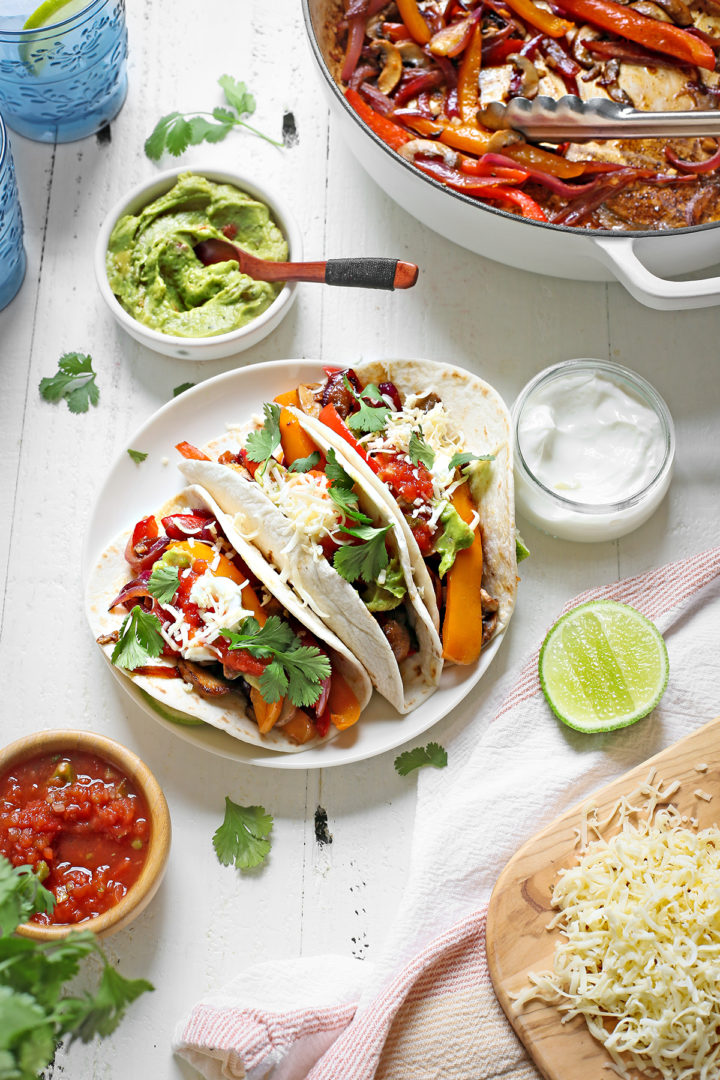 a white table set with a plate of vegetarian fajitas and bowls of salsa, guacamole, and sour cream