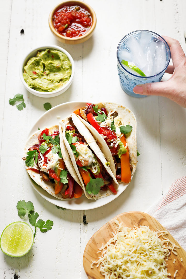 woman holding a glass of water with lime next to a plate of mushroom fajitas	