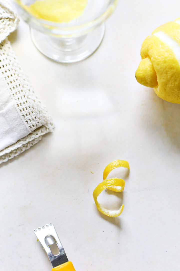 a channel knife, lemon twist, fresh lemon, and lemon cocktail on a white background