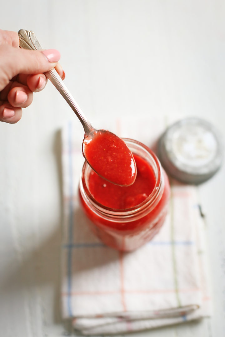 woman dipping a spoon in a jar of strawberry sauce