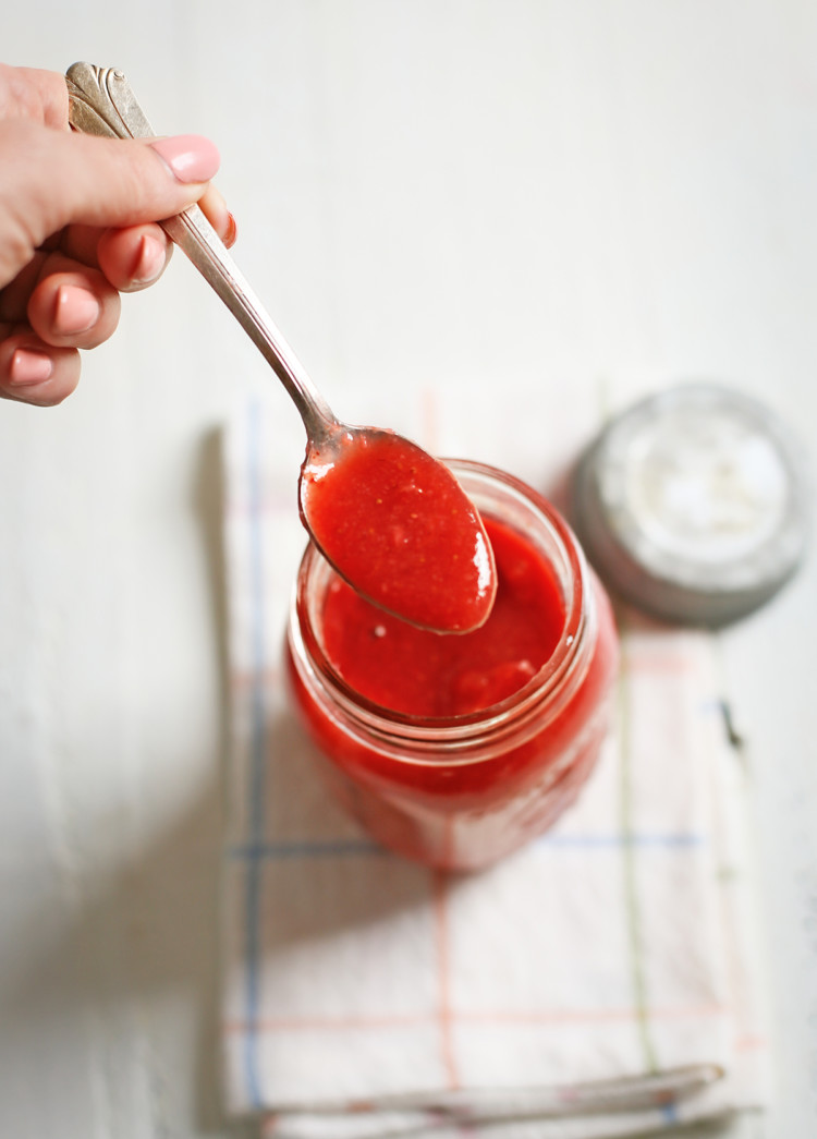 woman dipping a spoon in a jar of strawberry sauce to serve on waffles