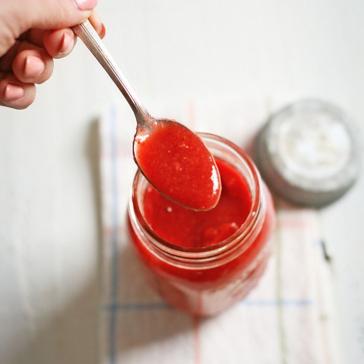 woman dipping a spoon in a jar of strawberry sauce to serve on waffles