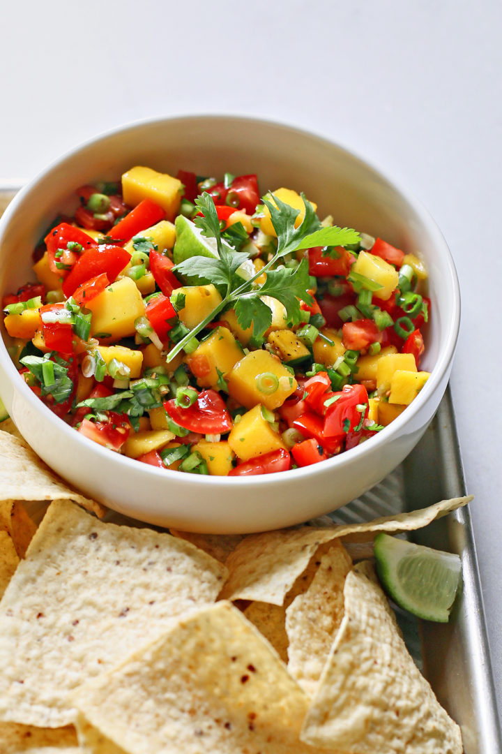 fresh tomato and mango salsa in a white bowl surrounded by tortilla chips on a metal tray