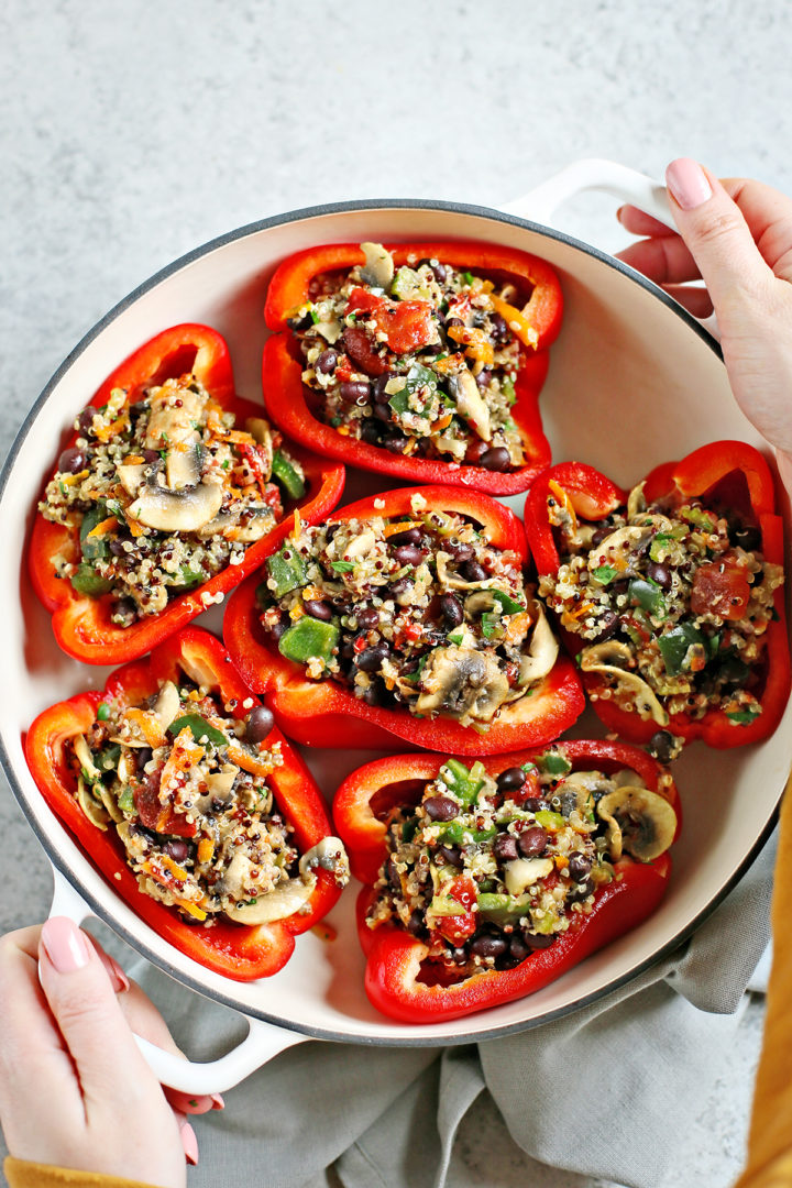 woman holding a baking pan with quinoa stuffed peppers before putting them in the oven to bake