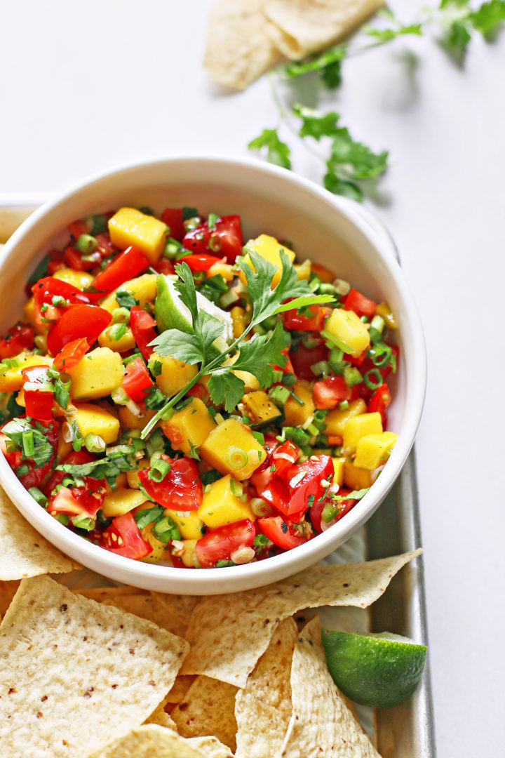 fresh mango salsa in a white bowl surrounded by tortilla chips on a metal tray