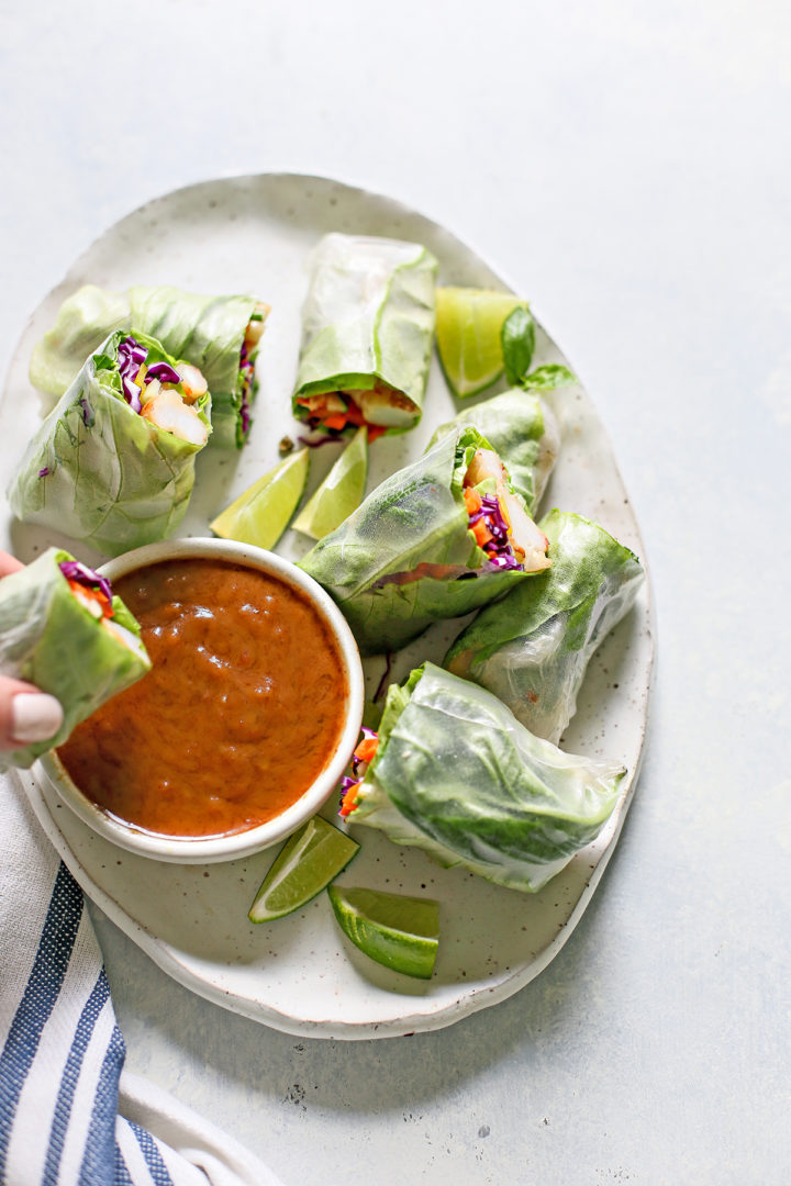 woman dipping a Vietnamese Spring Rolls in a bowl of spicy peanut dipping sauce