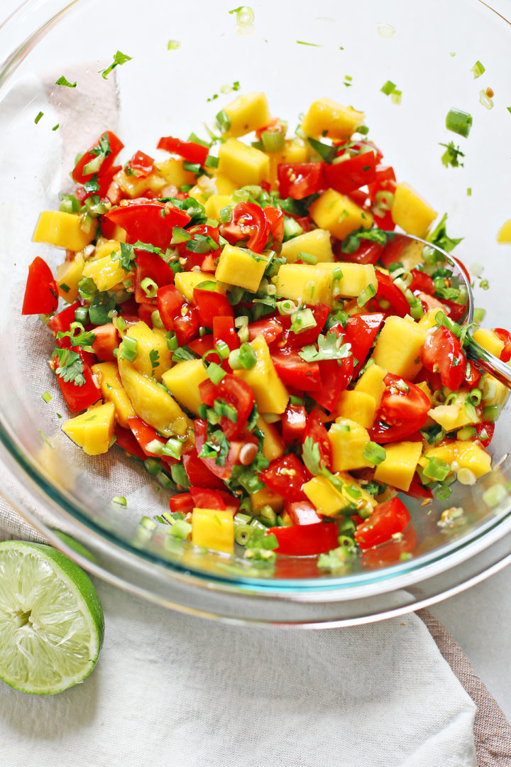 overhead photo of fresh tomato mango salsa in a glass bowl with a spoon