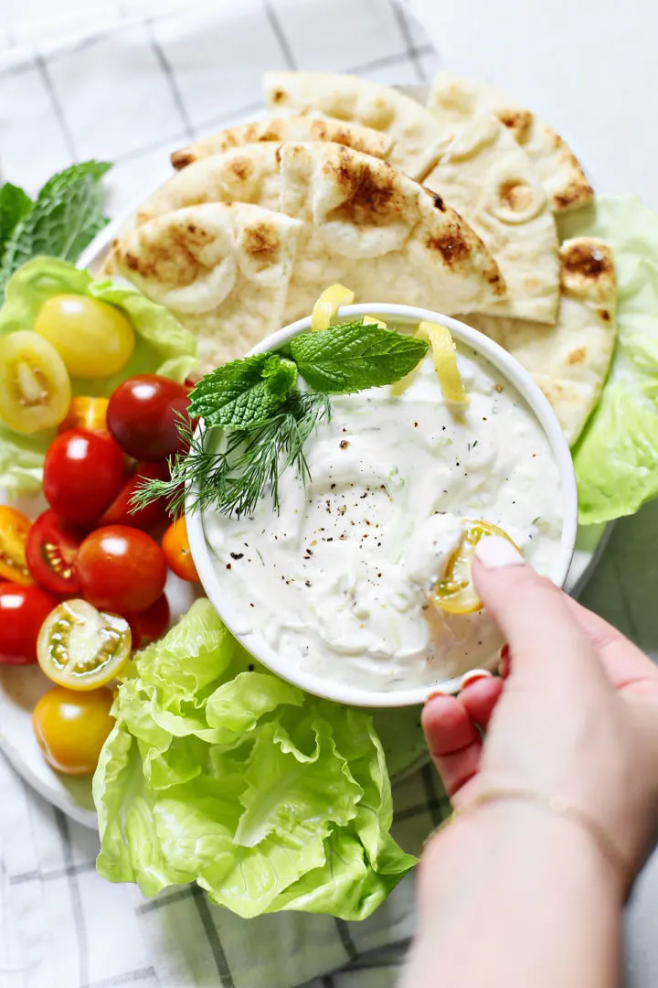 woman dipping vegetables in a bowl of tzatziki (a Greek sauce)