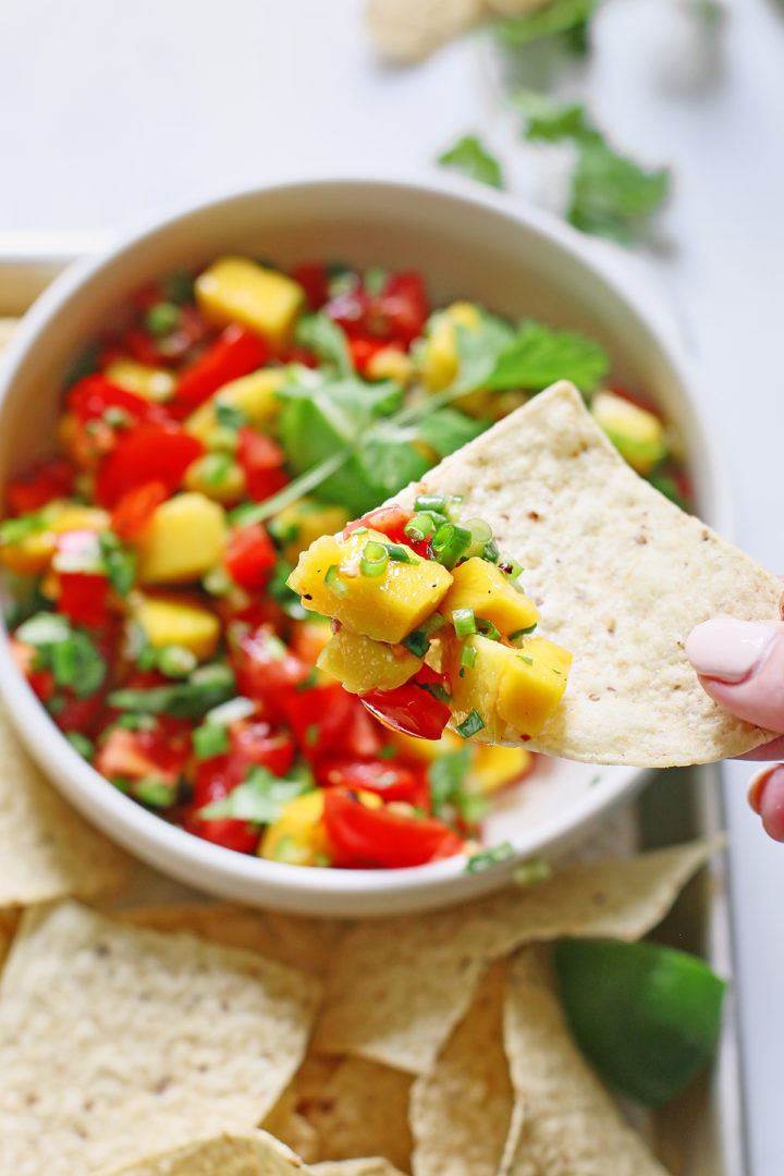 woman dipping a tortilla chip in a bowl of mango salsa