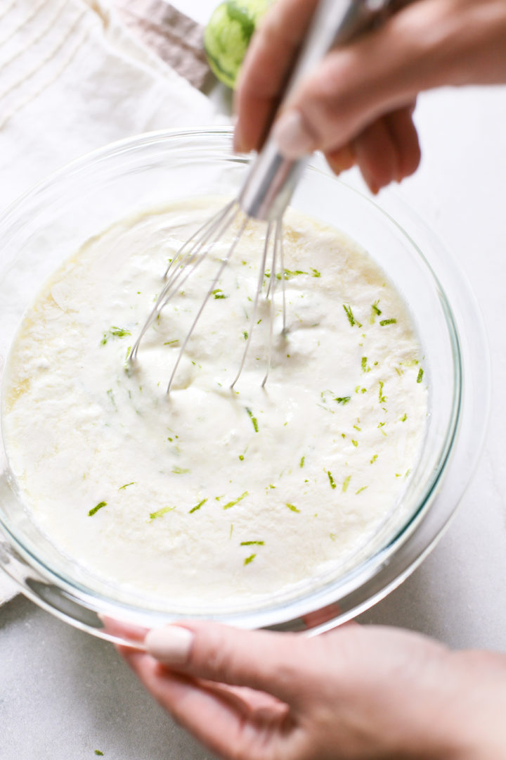 woman stirring ingredients for key lime ice cream with a whisk in a clear glass bowl