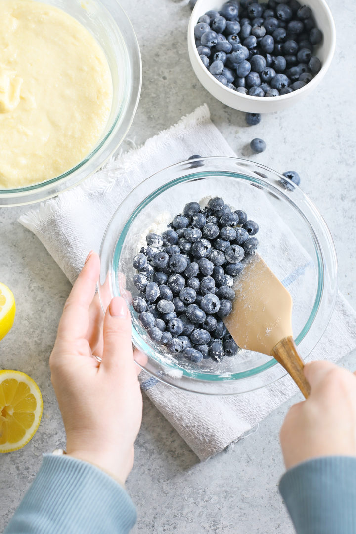 woman stirring blueberries in a glass bowl to make blueberry lemon bread