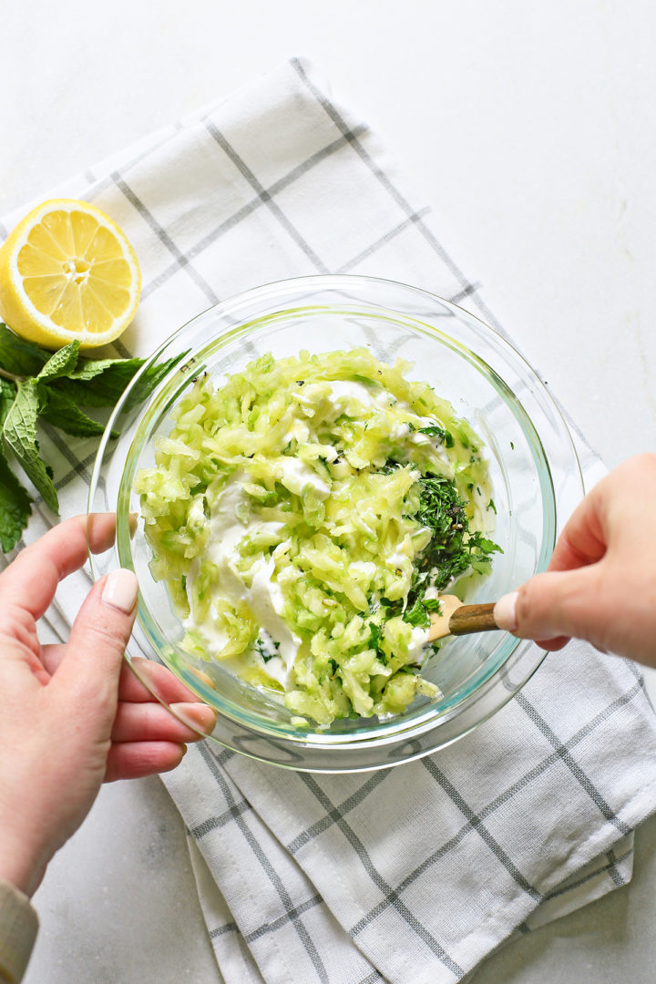 woman stirring ingredients in a glass bowl to make greek yogurt sauce	