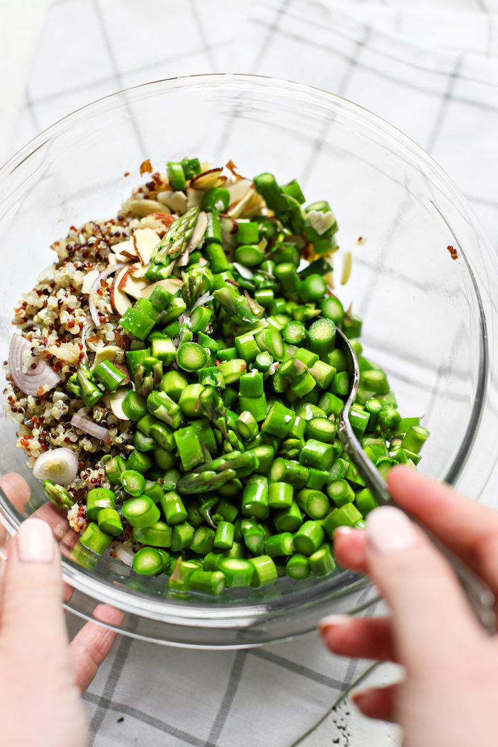 woman making asparagus salad in a clear glass bowl