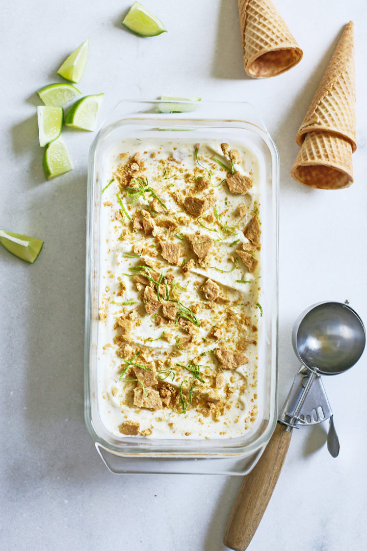 glass dish full of key lime ice cream with lime zest and graham cracker garnish on top sitting next to an ice cream scoop