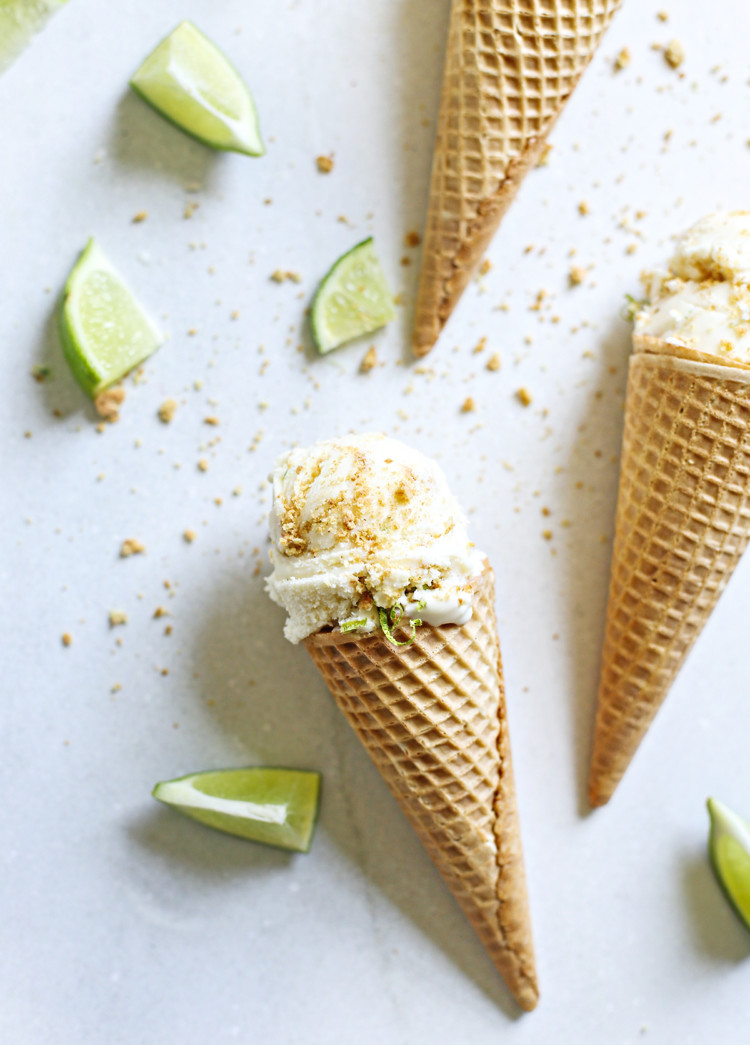 key lime pie ice cream served in ice cream cones with slices of lime and graham cracker crumb on a grey background