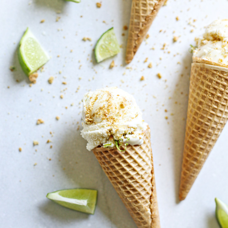 key lime pie ice cream served in ice cream cones with slices of lime and graham cracker crumb on a grey background