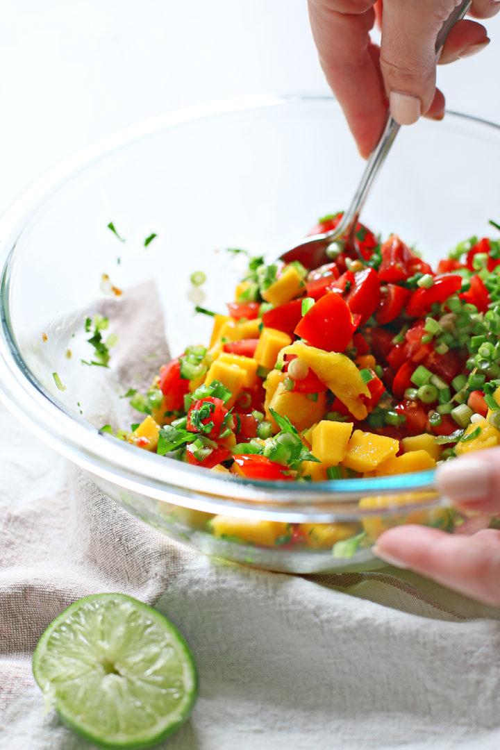 woman stirring a bowl of ingredients to make mango salsa with tomatoes