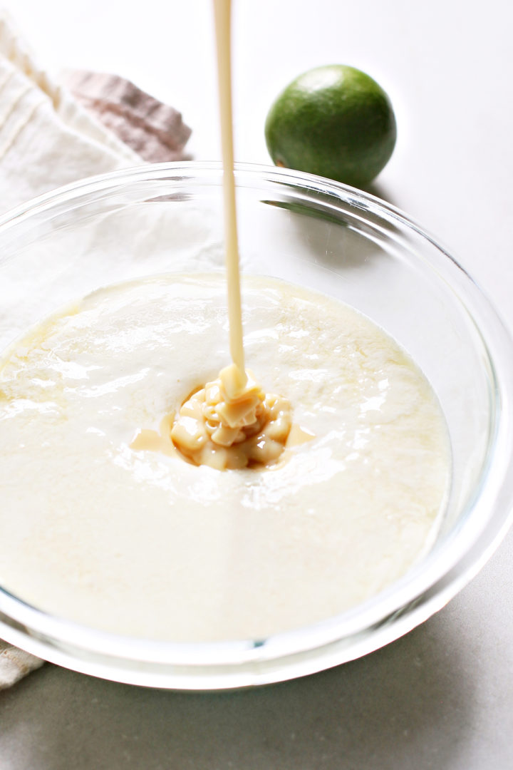 adding sweetened condensed milk for key lime ice cream recipe to a glass bowl with other ingredients