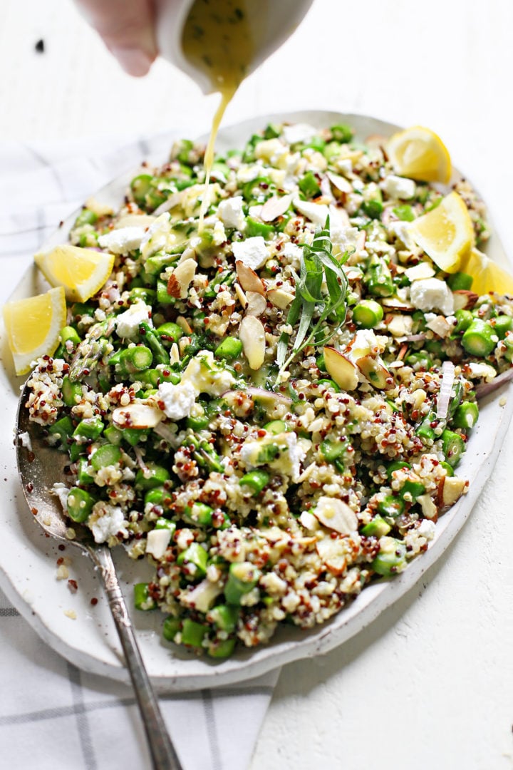 woman pouring tarragon vinaigrette onto a platter of cold asparagus salad