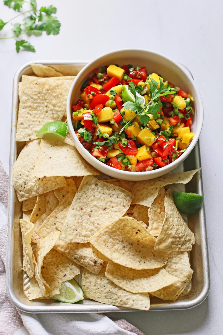 fresh tomato mango salsa in a white bowl surrounded by tortilla chips on a metal tray