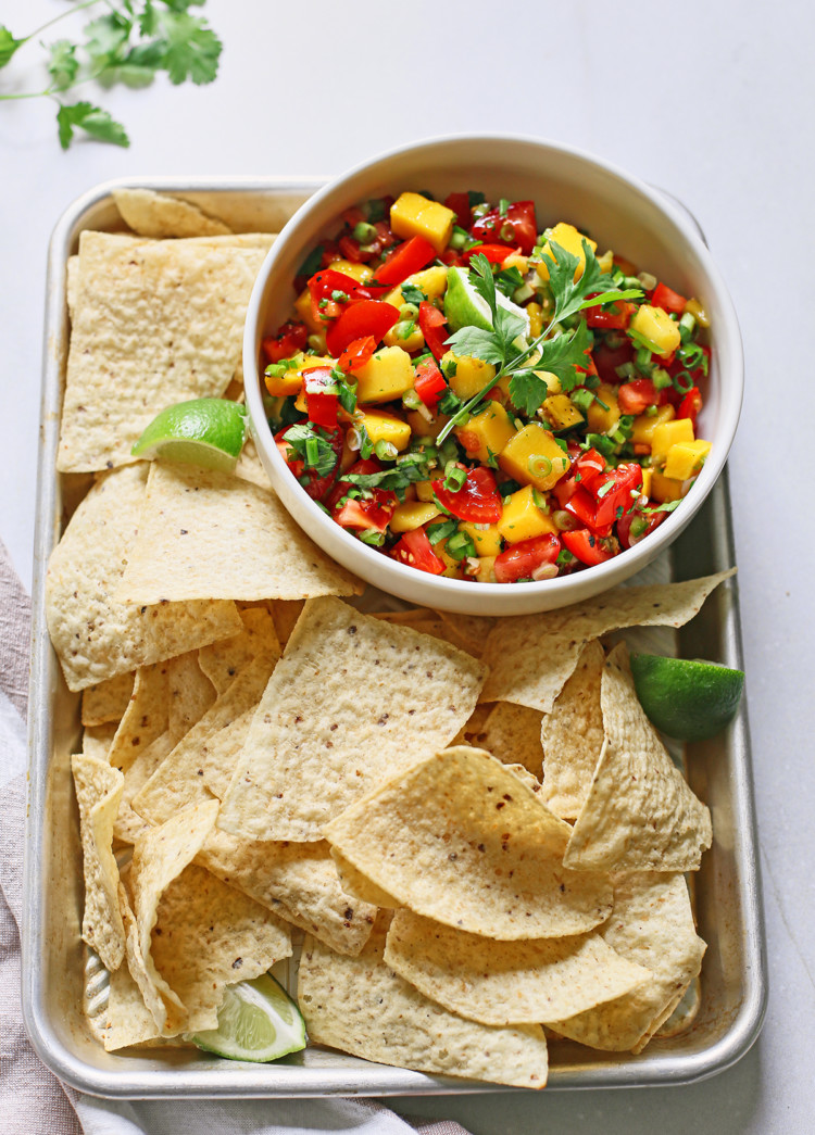 fresh mango salsa in a white bowl surrounded by tortilla chips on a metal tray