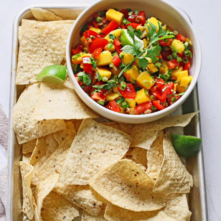 fresh mango salsa in a white bowl surrounded by tortilla chips on a metal tray