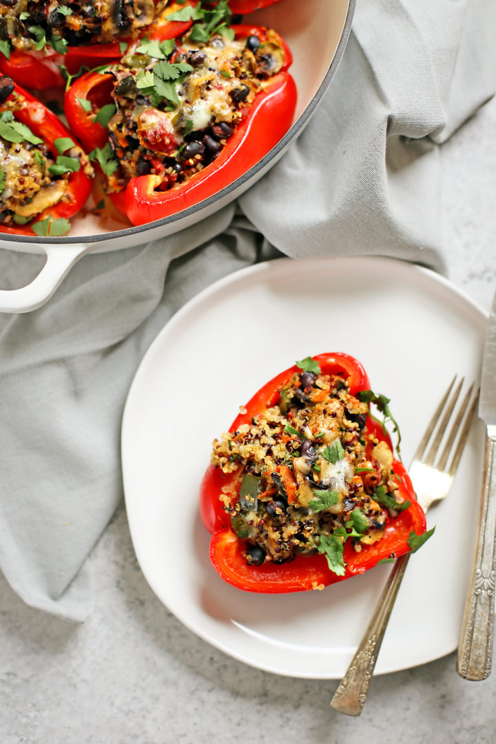 white plate with a quinoa stuffed bell pepper on it next to a fork and knife