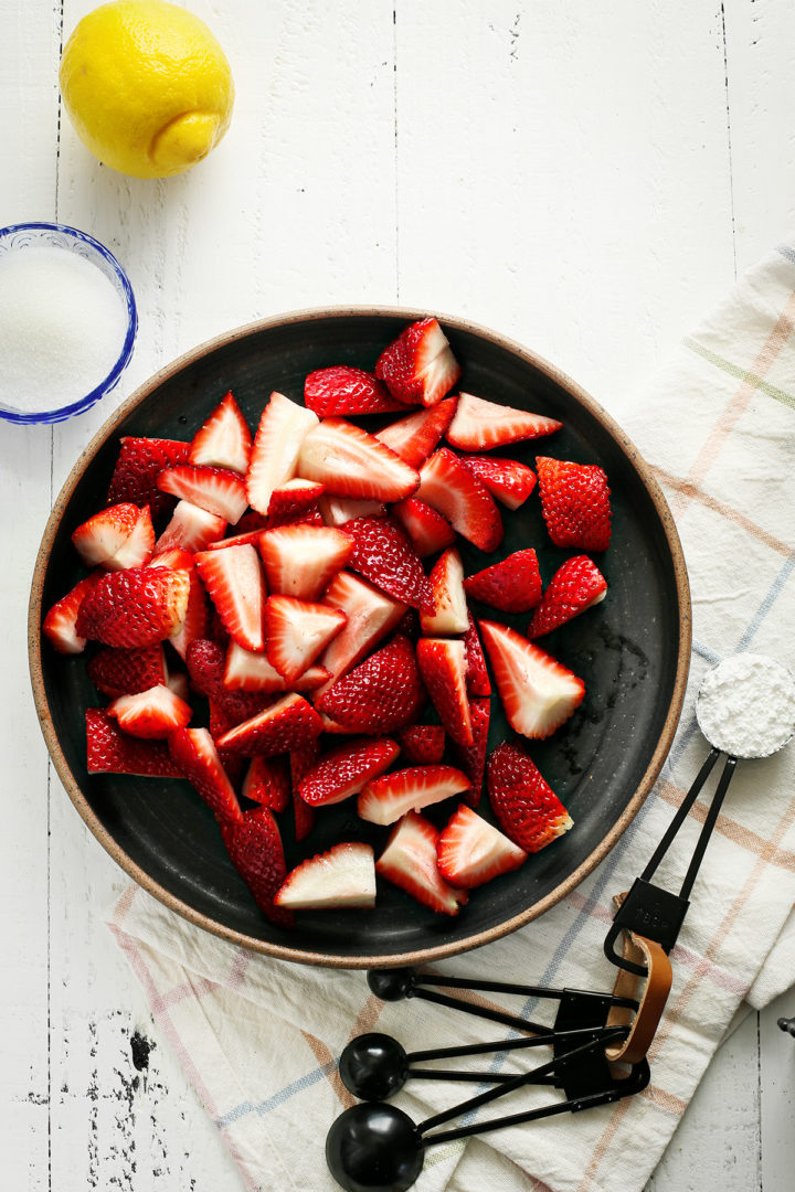 ingredients needed to make a recipe for strawberry sauce arranged on a white wooden table