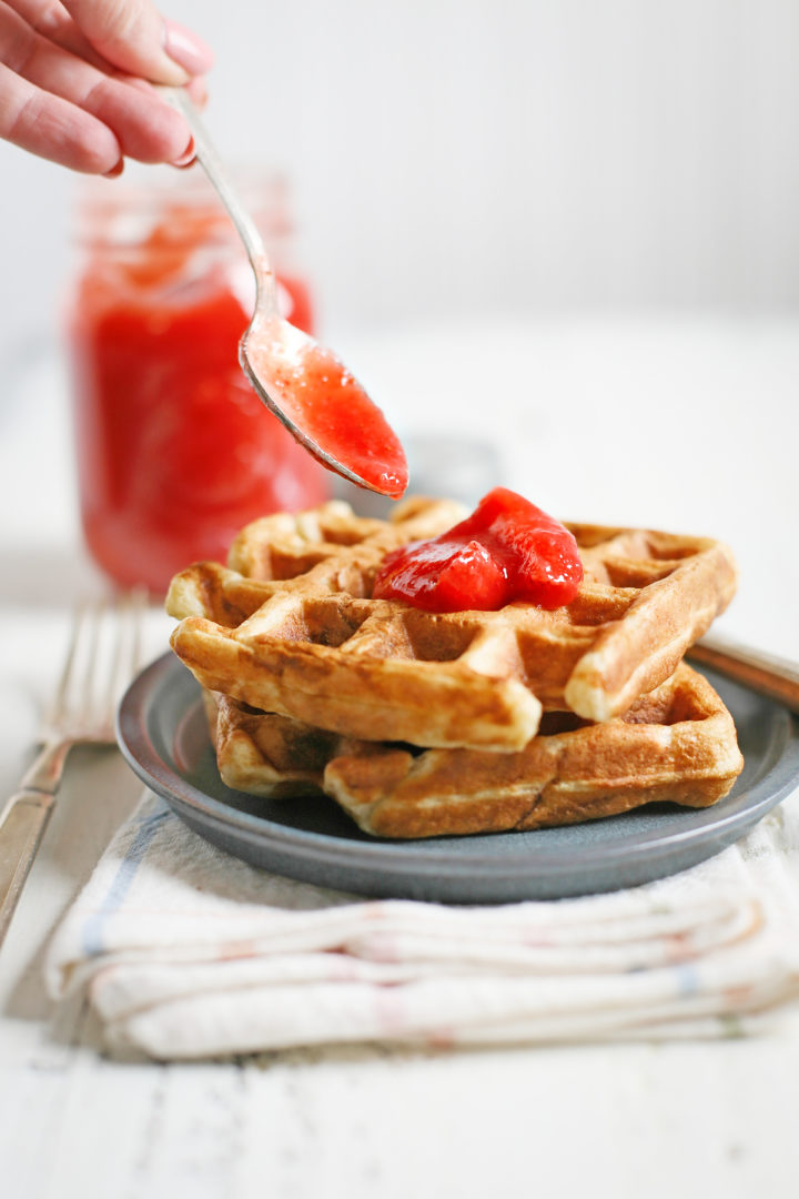 woman spooning fresh strawberry topping onto a plate of waffles