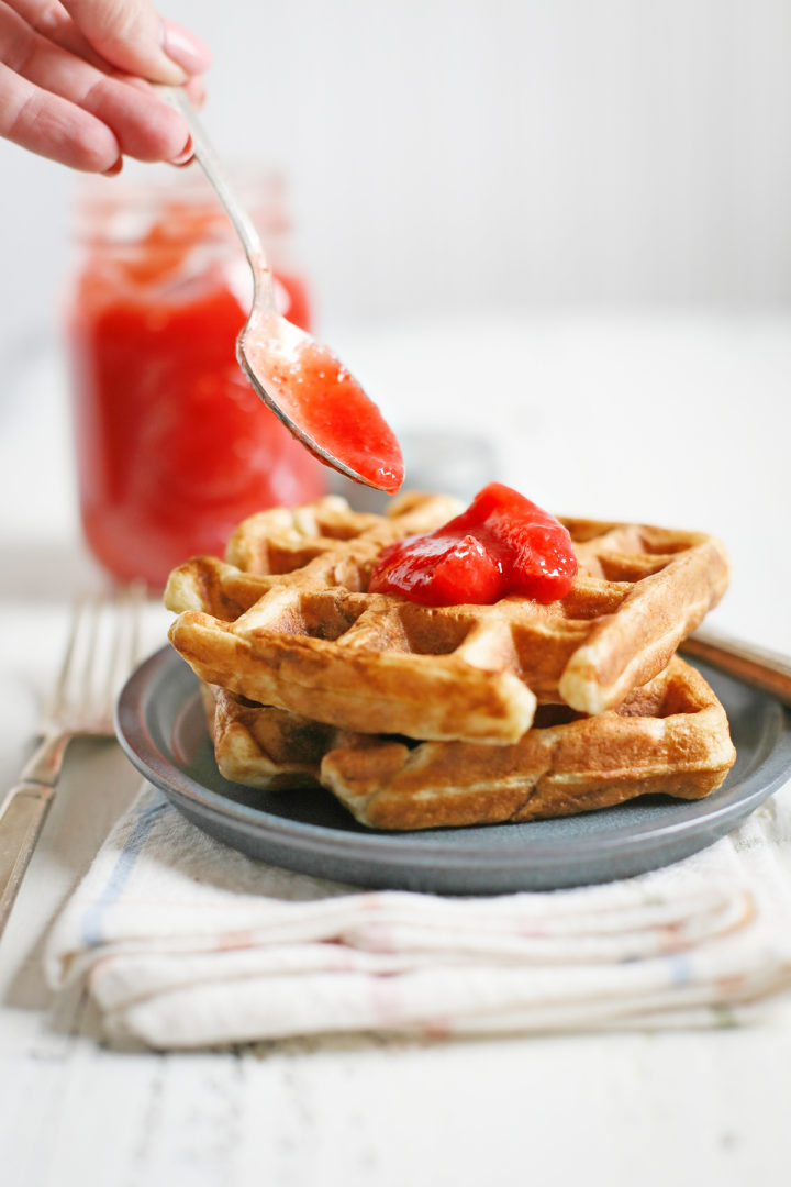 woman spooning fresh strawberry topping onto a plate of waffles