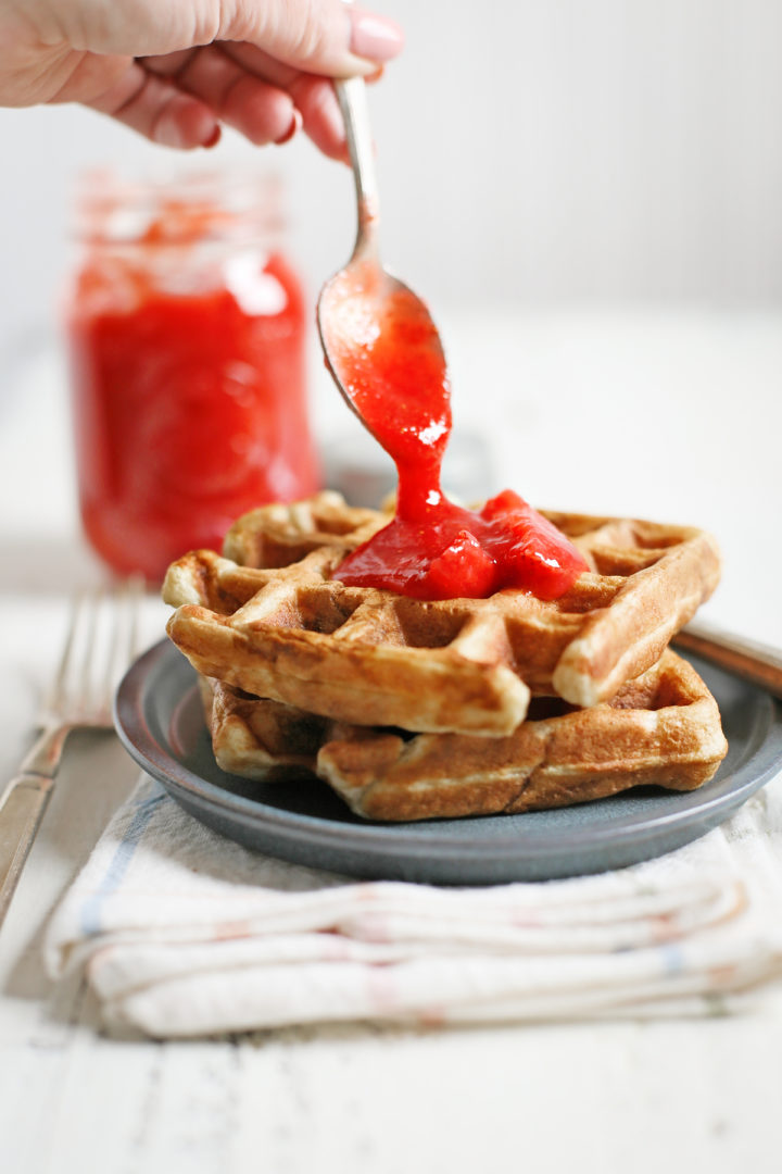woman spooning strawberry sauce onto a plate of homemade waffles