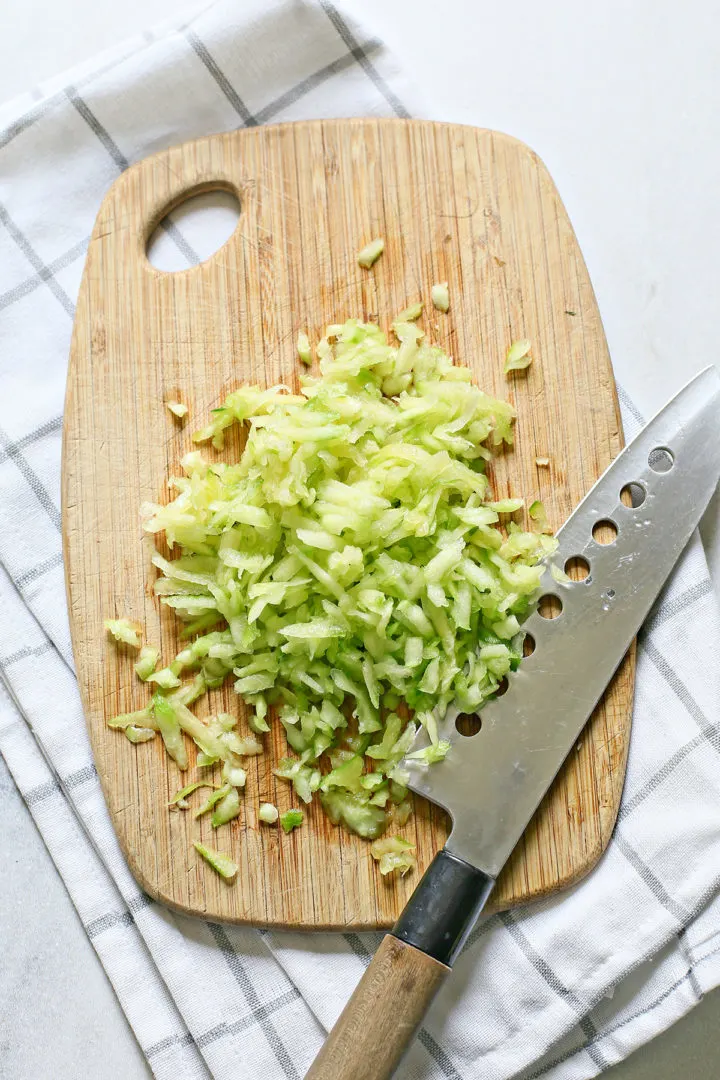 chopped up cucumber on a cutting board with a knife to make tzatziki dip	