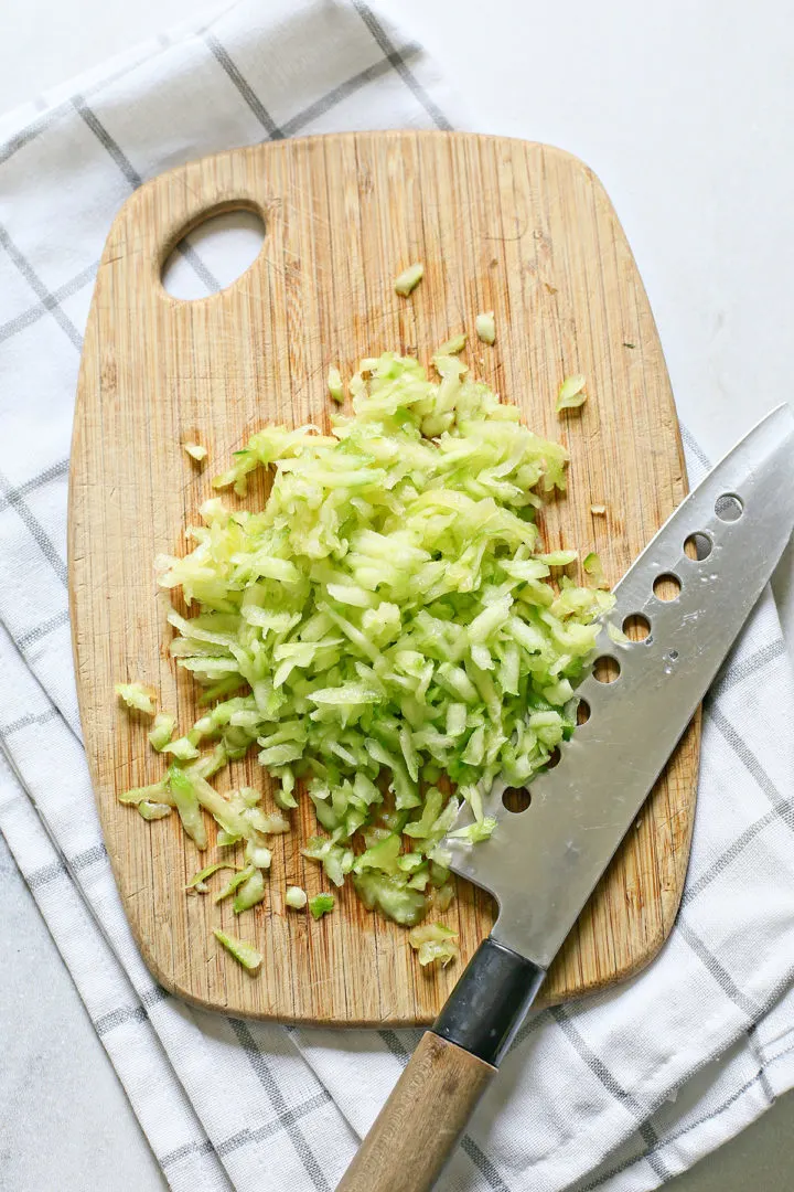 chopped up cucumber on a cutting board with a knife to make tzatziki dip