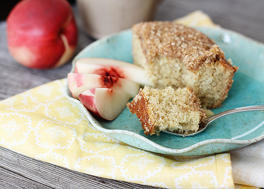 slice of banana snack cake on a blue plate next to nectarine slices with a fork cutting a bite out of the banana cake