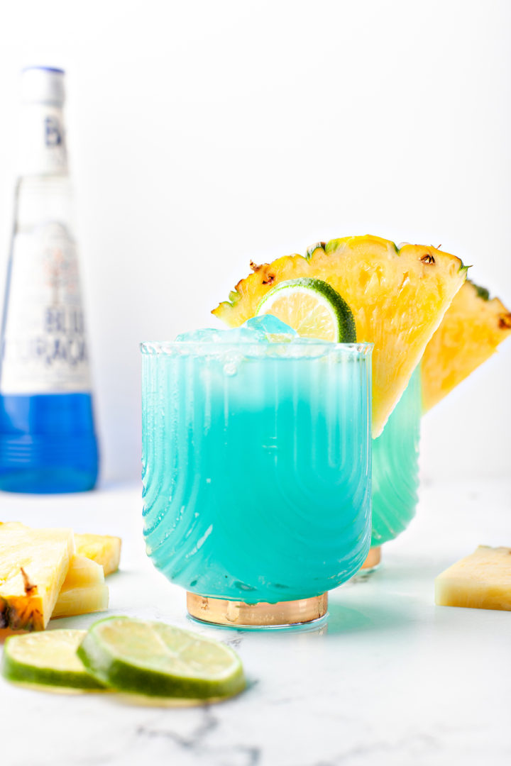 blue hawaiian cocktail in two glasses next to a bottle of blue curacao 