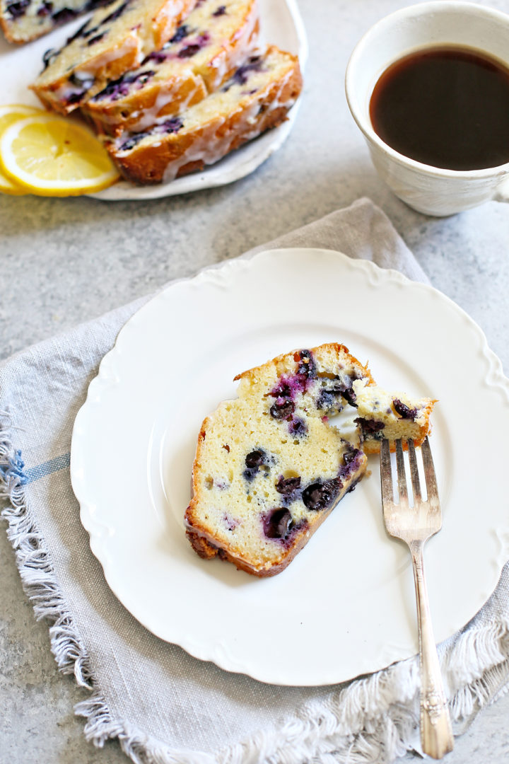 a slice of lemon blueberry bread on a white plate with a fork next to it