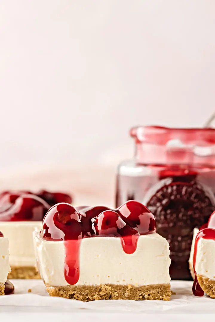 side view of cherry cheesecake bars with cherry pie filling on top