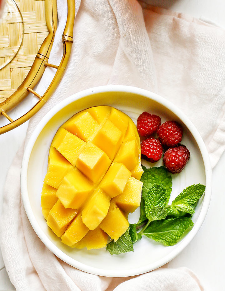 hedgehog cut mango on a white plate with raspberries and fresh mint