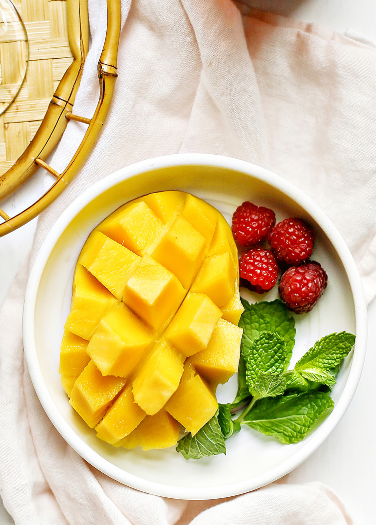 hedgehog cut mango on a white plate with raspberries and fresh mint