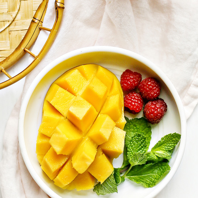 hedgehog cut mango on a white plate with raspberries and fresh mint