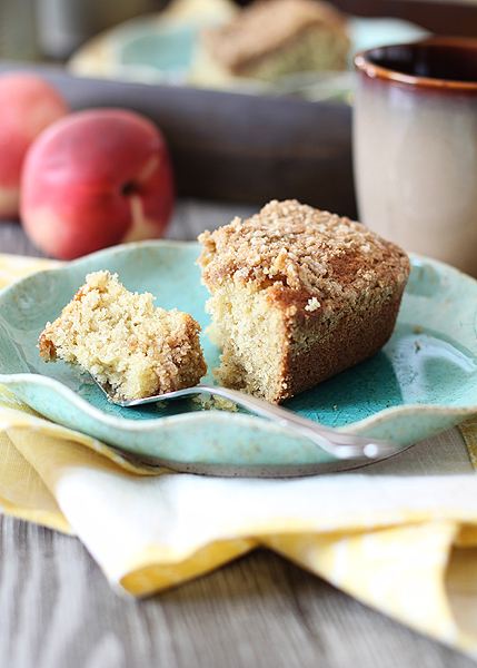 close up of a slice of banana snack cake with streusel topping on a blue plate on a wooden table with coffee mug