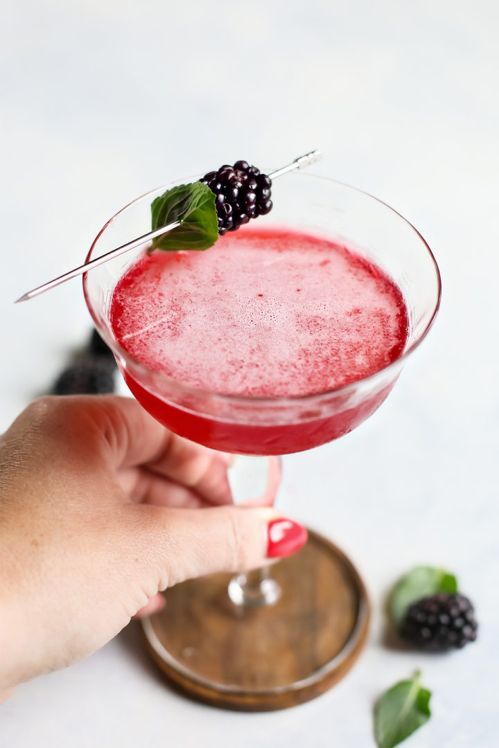 woman holding a cocktail glass with blackberry simple syrup and fresh blackberry