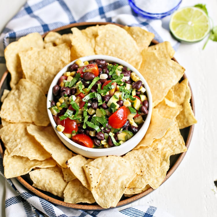 overhead photo of a white bowl of zucchini salsa with tortilla chips surrounding it