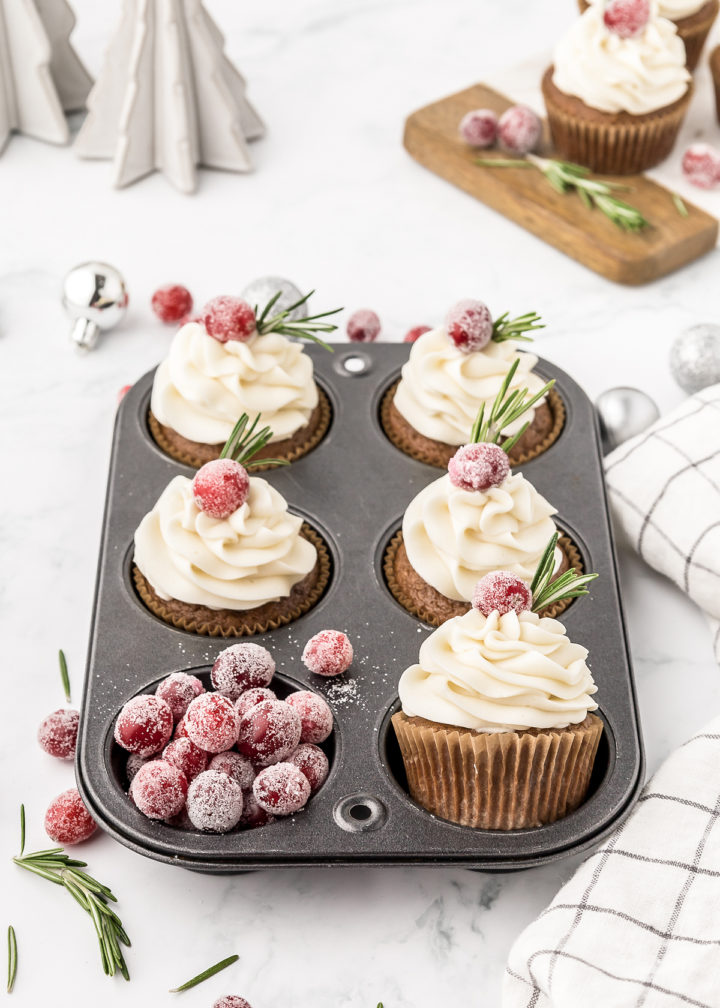 frosted gingerbread cupcakes in a muffin tin with sugared cranberry cupcake garnishes