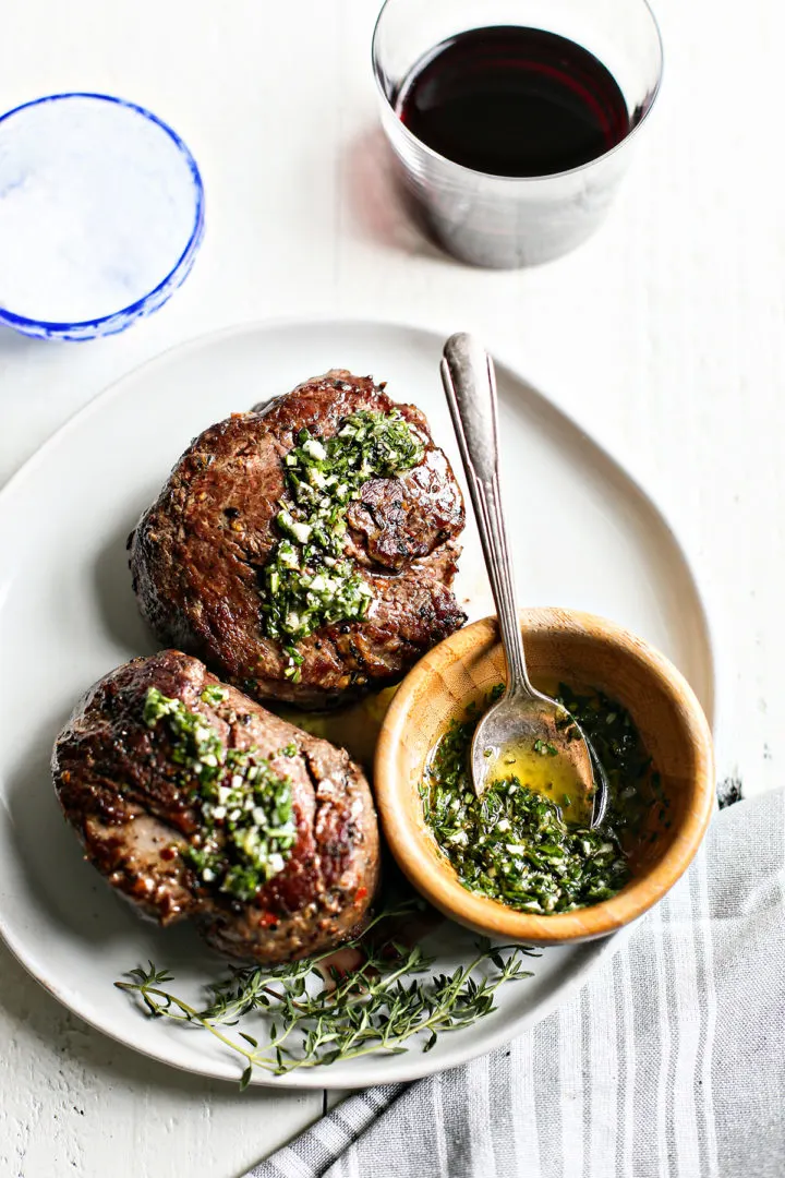 overhead photo of a plate of two steaks with gremolata sauce on top