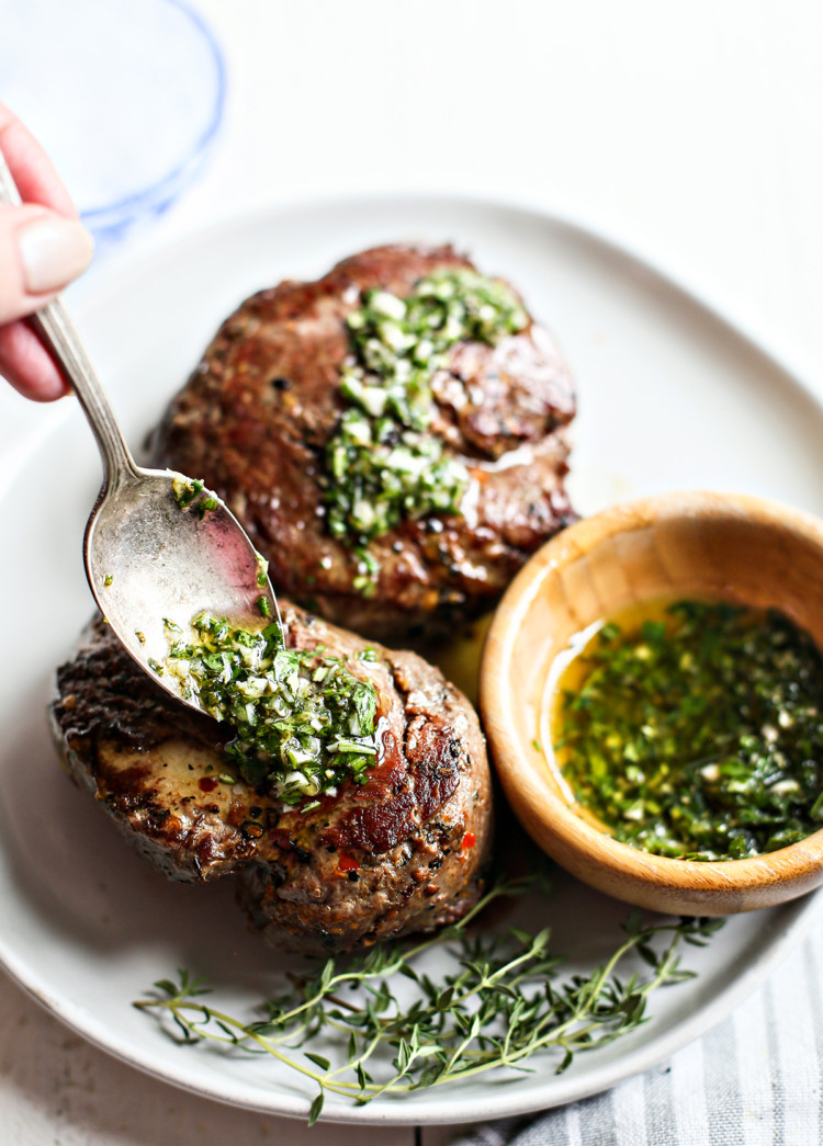 woman spooning gremolata sauce onto seared steaks