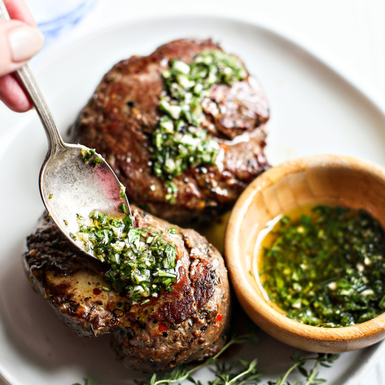 woman spooning gremolata sauce onto seared steaks