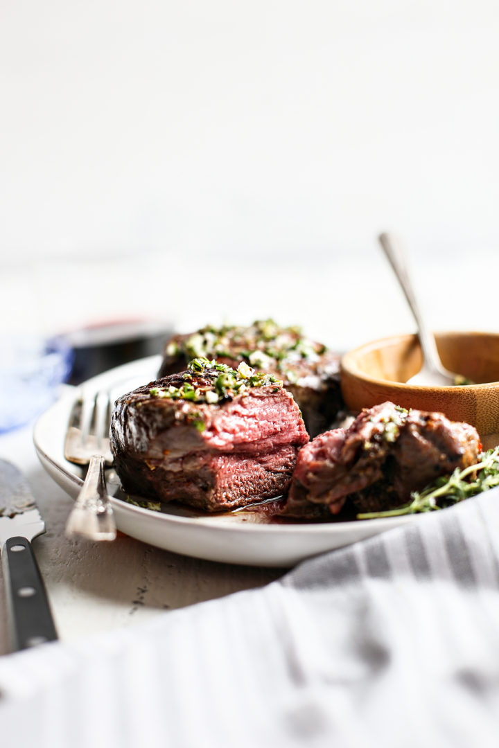 a partially eaten steak on a plate with a fork and bowl of gremolata sauce