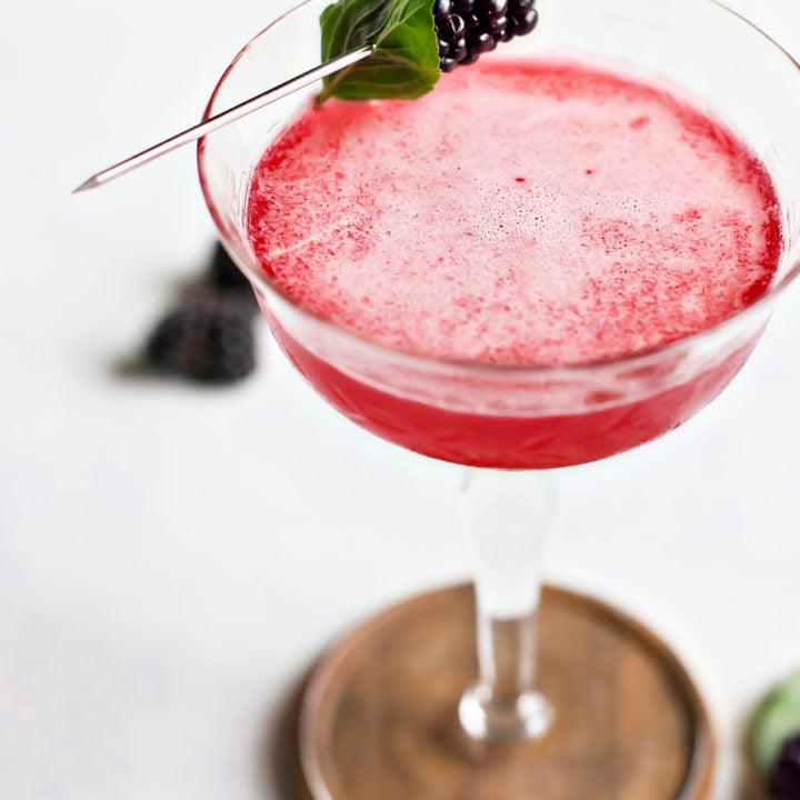 close up of blackberry simple syrup in a cocktail glass with fresh blackberries and basil